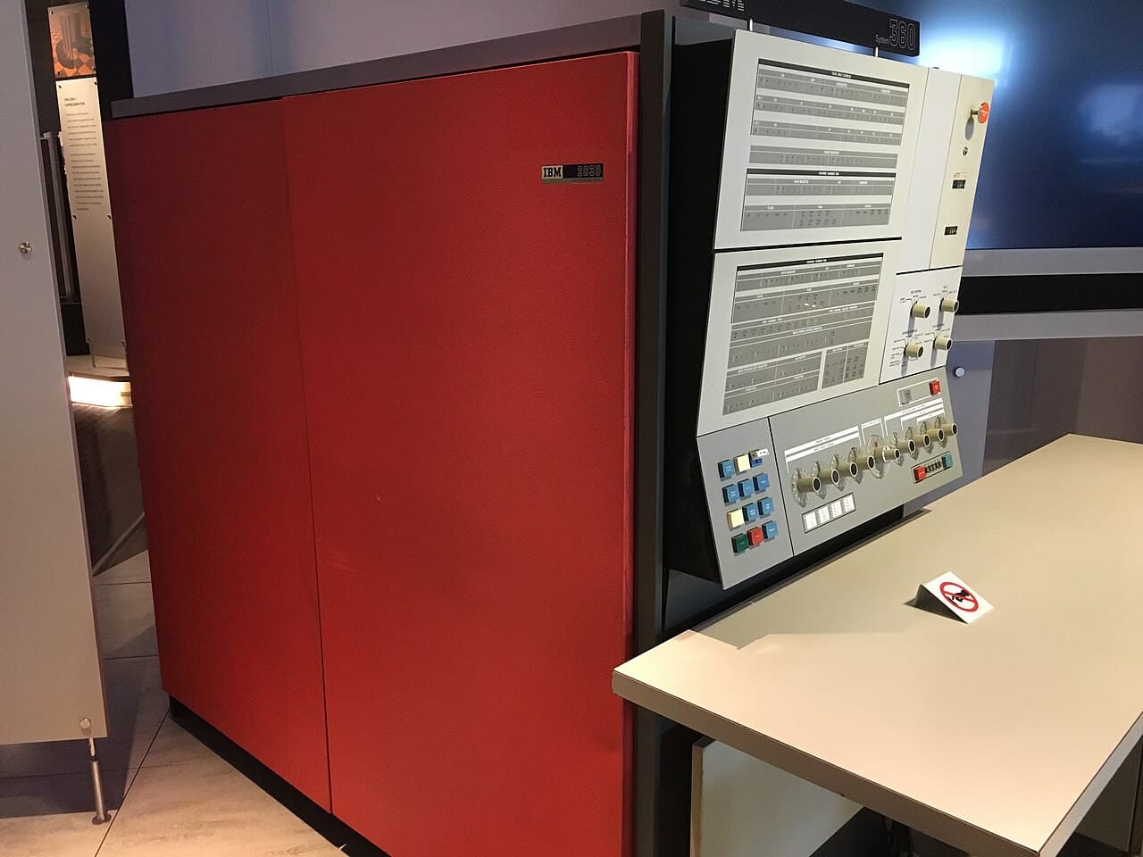An IBM System/360 Model 30 in a museum: a tall red cabinet beside a grey operator panel full of dials and switches.